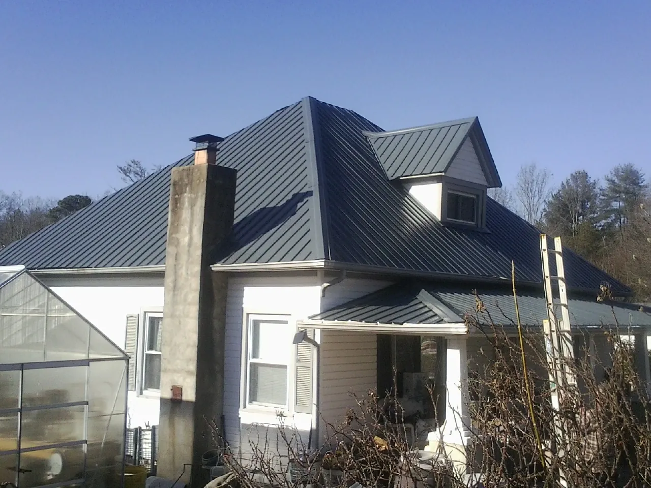 Dark blue standing seam metal roof on a white farmhouse with dormer — Slate & Tile Roof Repair by Roofing Brothers in Davidson