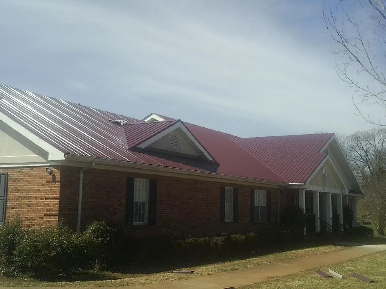 Red metal roof with gabled entries on a long brick building, from a Hail Damage Roof Repair job in Davidson