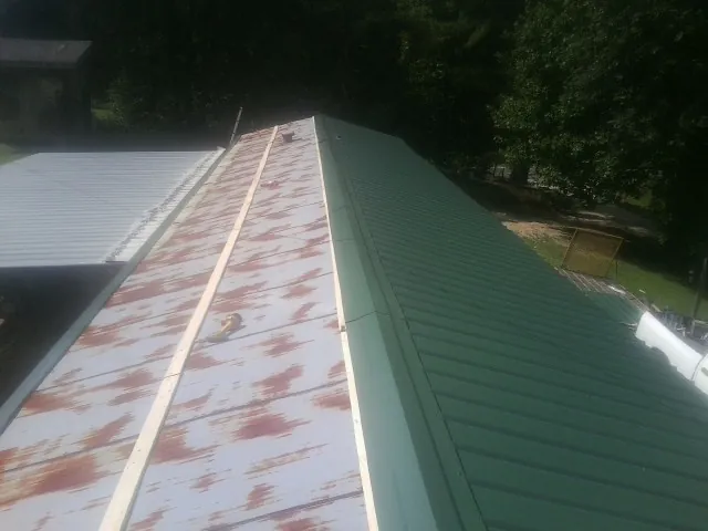 Old rusted panels beside newly installed green metal roofing — Wind Damage Roof Repair by Roofing Brothers in Davidson