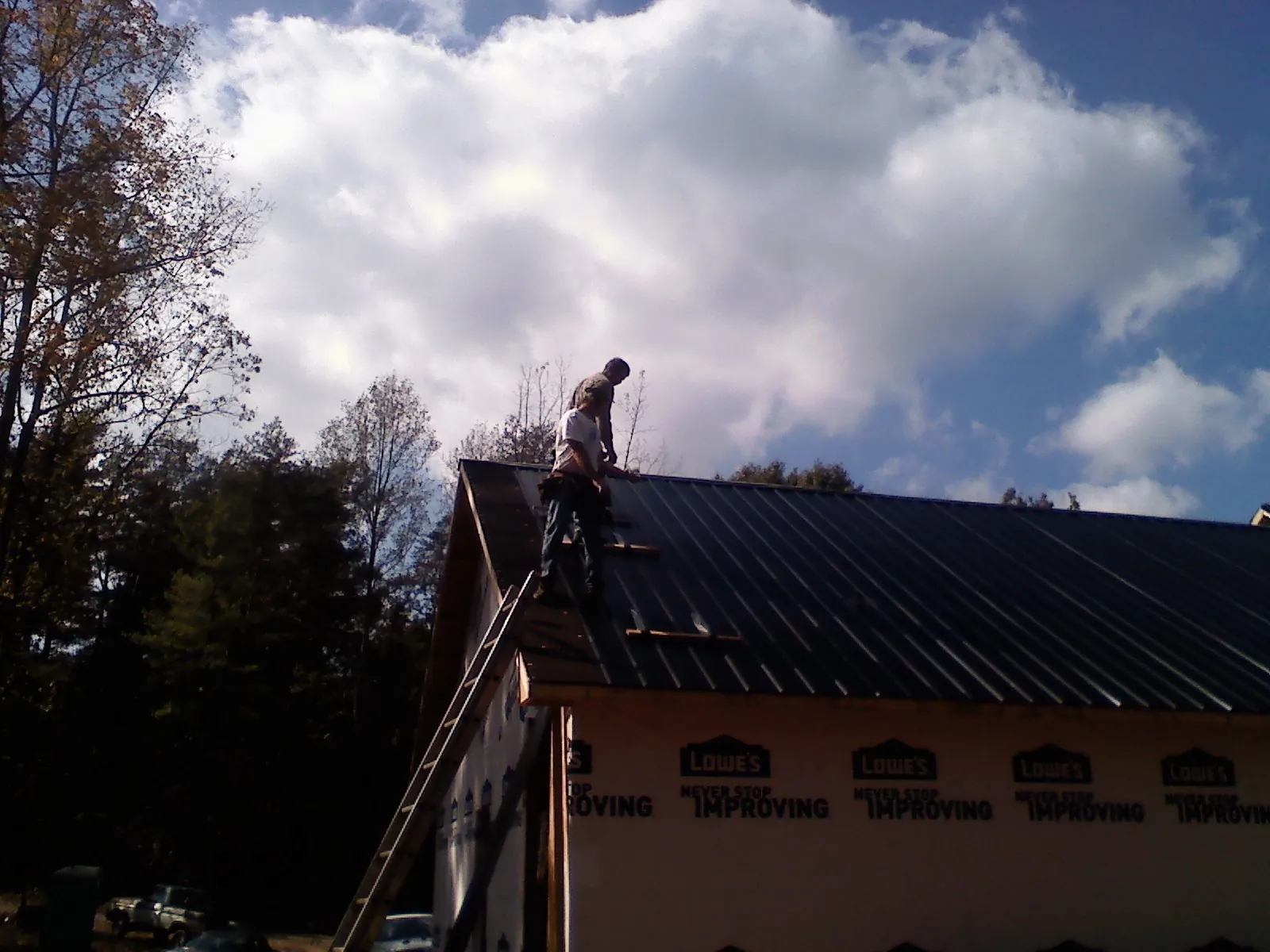 Roofer fastening dark metal panels high against a cloudy sky, from a Roof Inspection job in Davidson