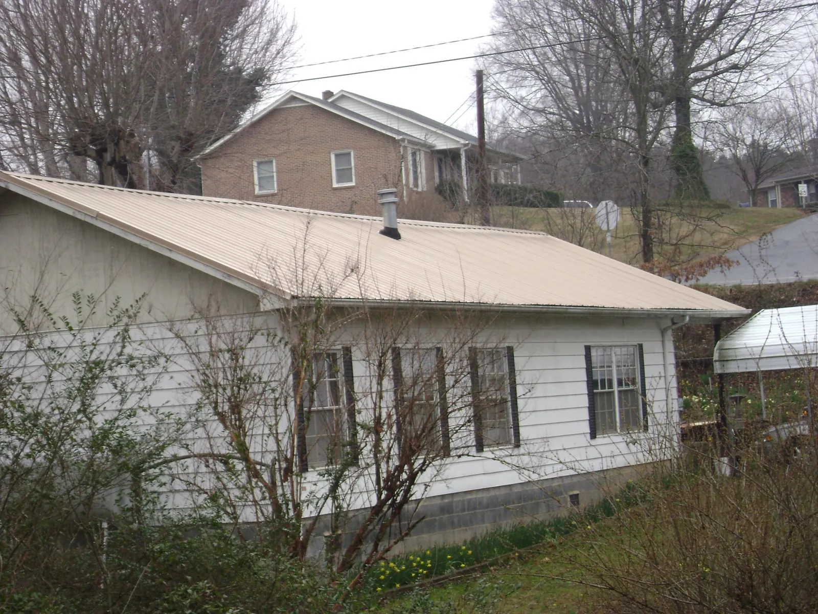 Tan metal roof on a white sided house set into a hillside — Commercial Roofing by Roofing Brothers in Davidson